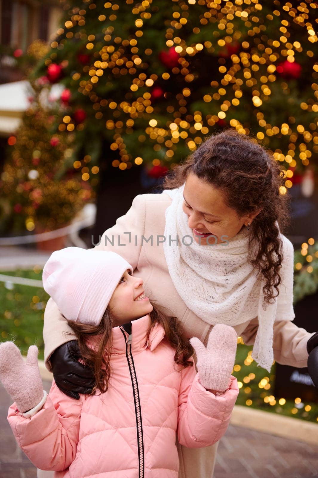 Mother and little daughter smile, enjoying together happy winter holidays, standing by illuminated Christmas tree by artgf