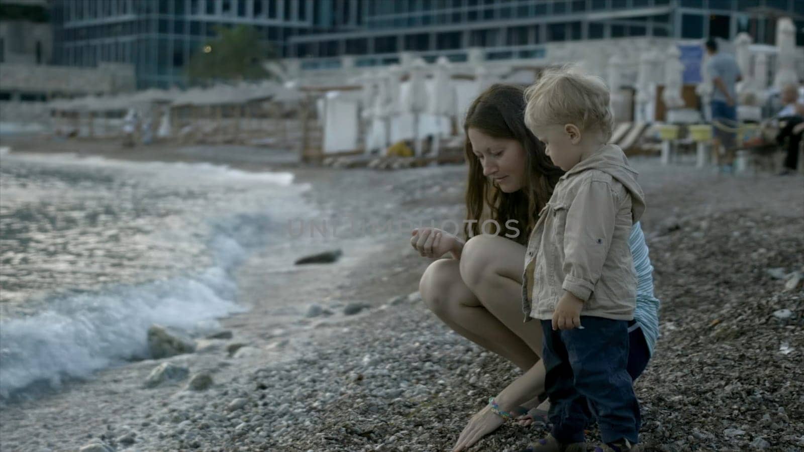 Mom and child throw stones into sea. Creative. Mother and child are relaxing at sea and playing on beach with stones. Mother and child are resting on shore throwing stones.