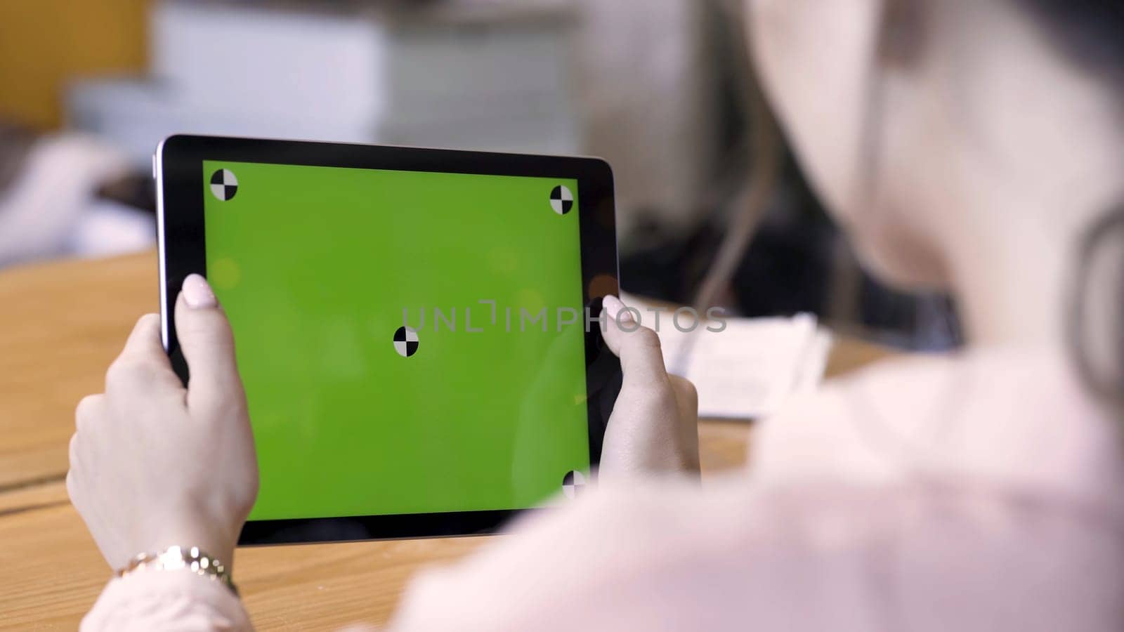 Rear view of a woman holding a tablet with chromakey with tracking marks on wooden table background. Stock footage. Different action with the device in daylight indoor space, green screen. by Mediawhalestock