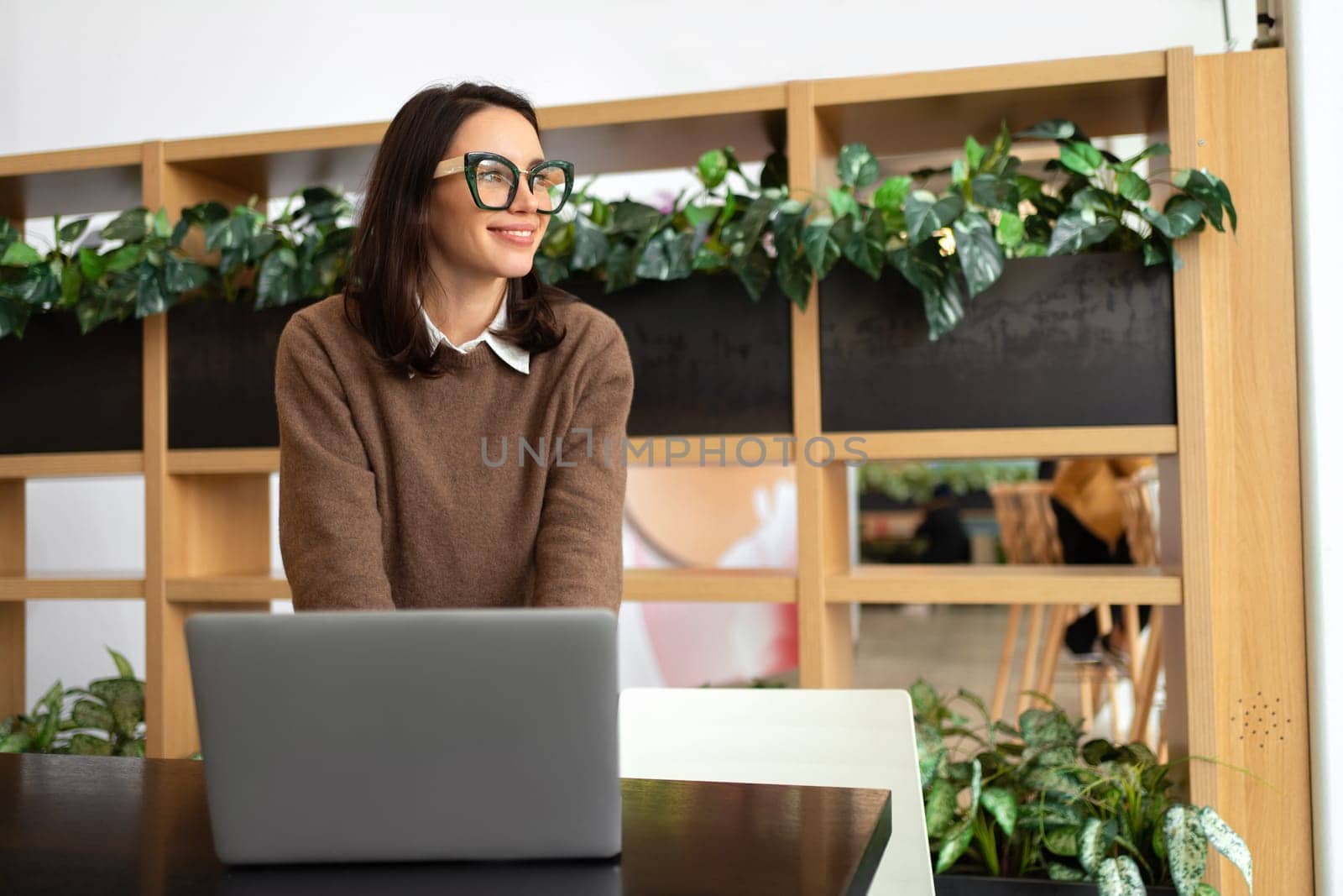 Woman with eyeglasses stands in an office at desk and looks away by andreonegin