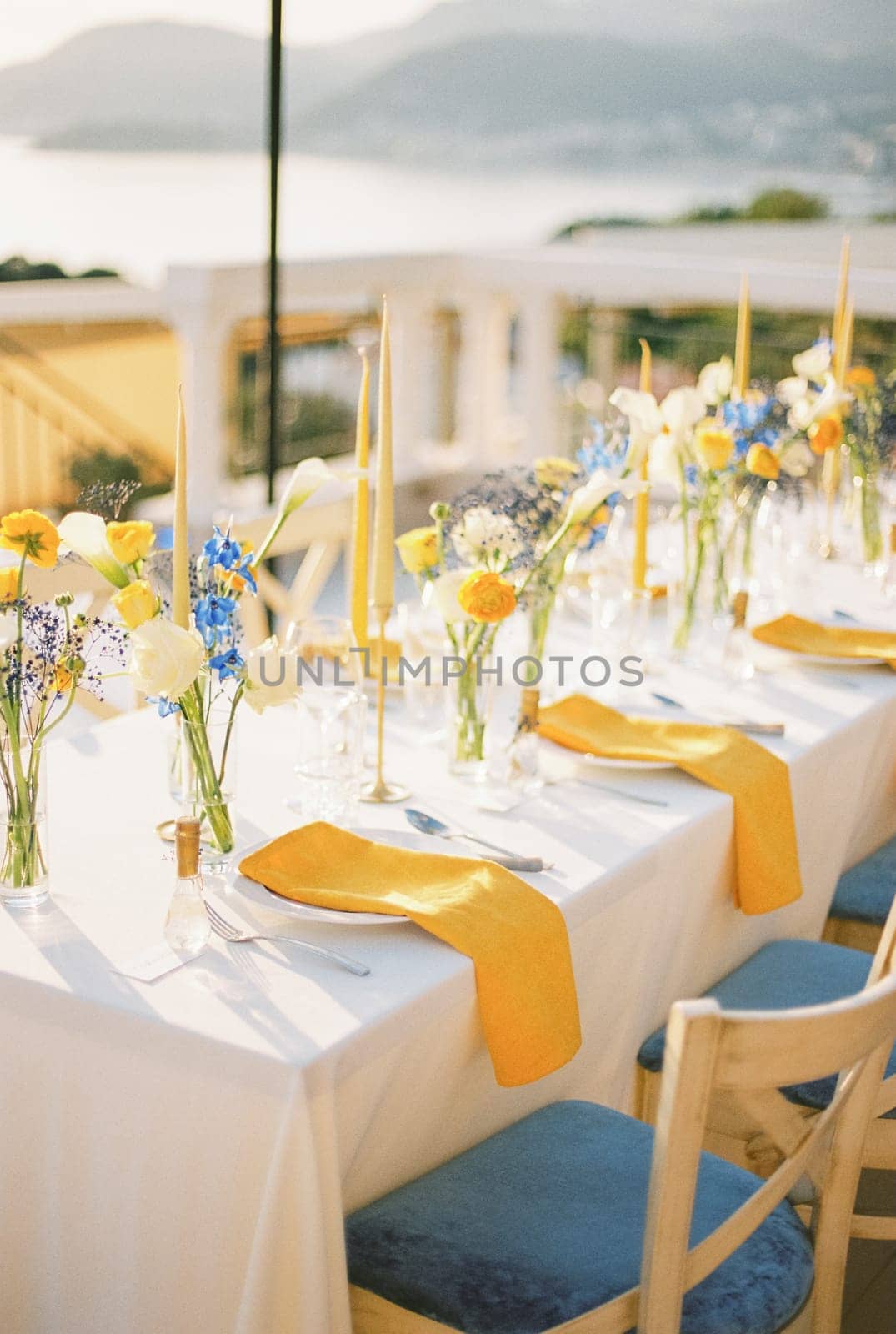 Long festive table with bouquets of flowers and yellow napkins on plates. High quality photo