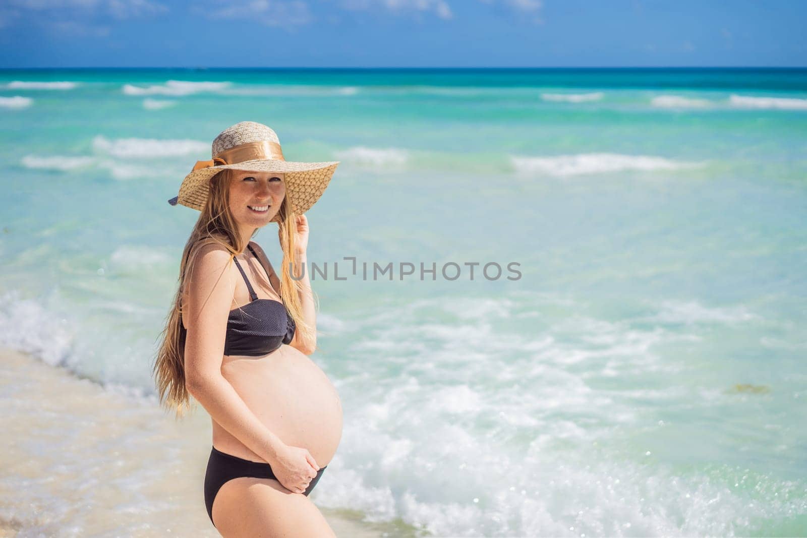 Radiant and expecting, a pregnant woman stands on a pristine snow-white tropical beach, celebrating the miracle of life against a backdrop of natural beauty.