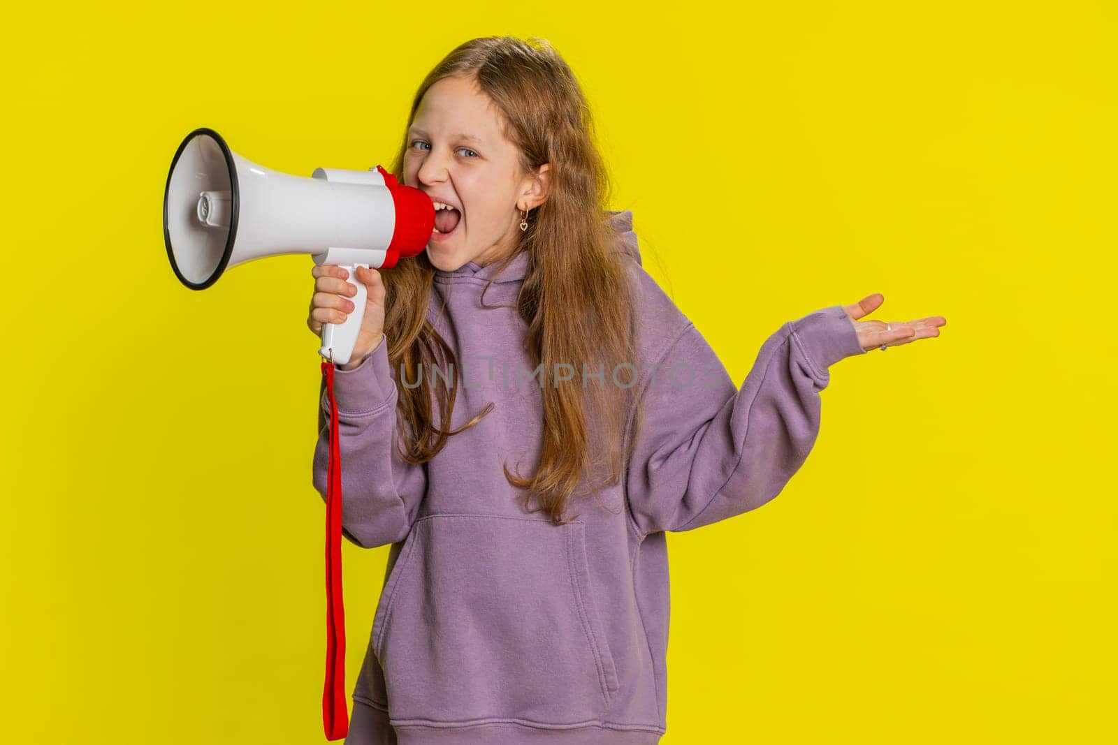 Young preteen child girl kid talking with megaphone, proclaiming news, loudly announcing advertisement discounts sale using loudspeaker to shout speech. Teenager children isolated on yellow background