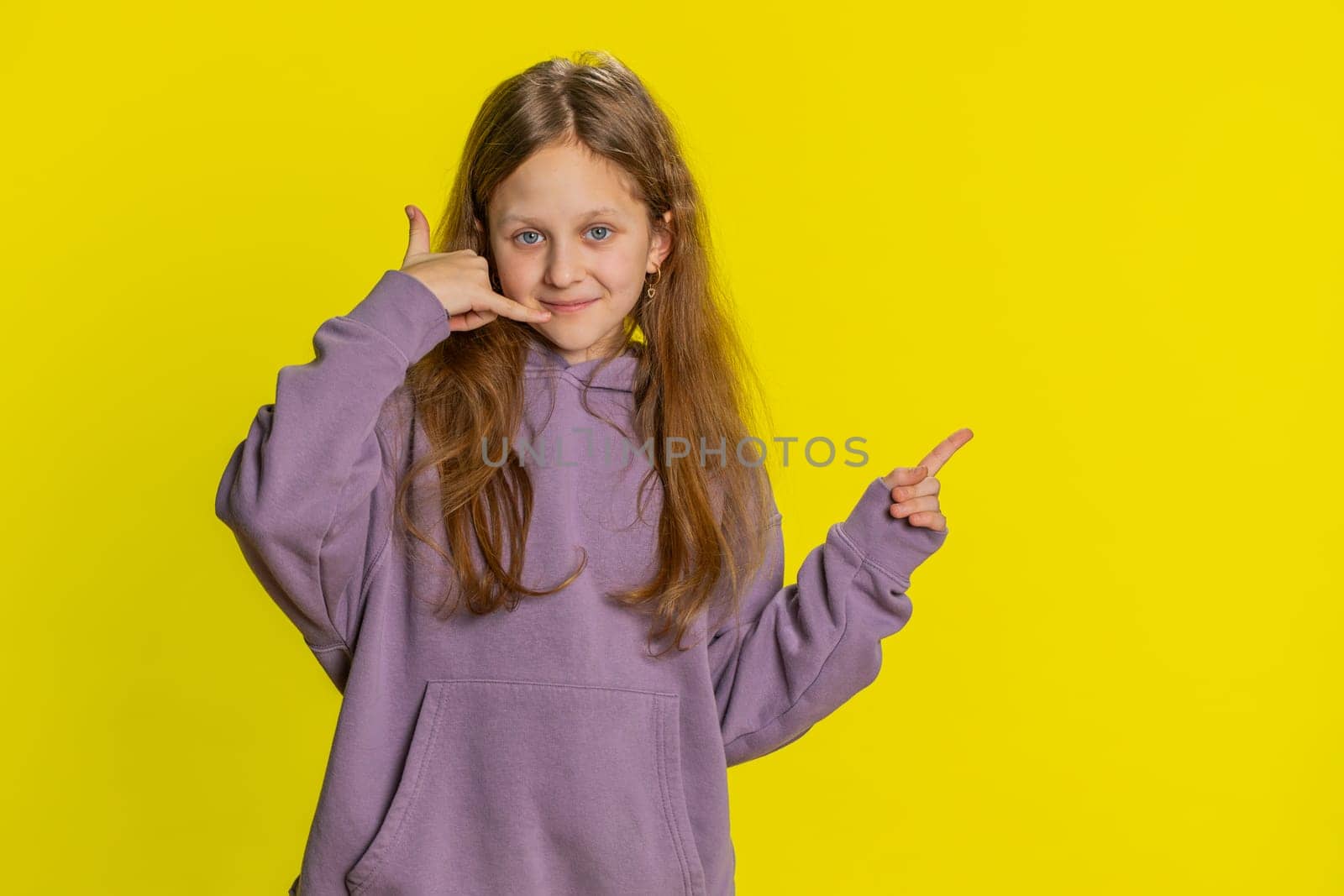 Call me, here is contact number. Preteen child girl kid looking at camera doing phone gesture, asking for conversation. Hotline online service proposition advertisement. Children on yellow background