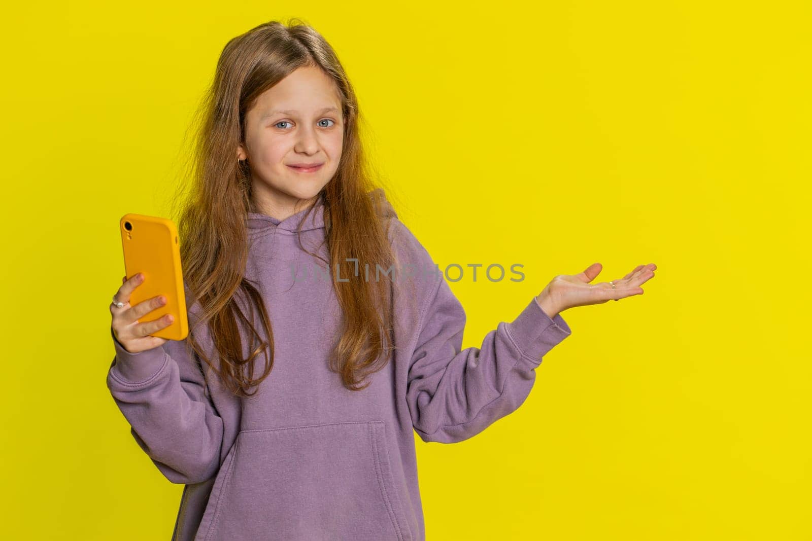 Young preteen child girl kid with mobile smartphone showing pointing empty place, advertising area for commercial text, copy-space for apps promotion. Teenager children isolated on yellow background