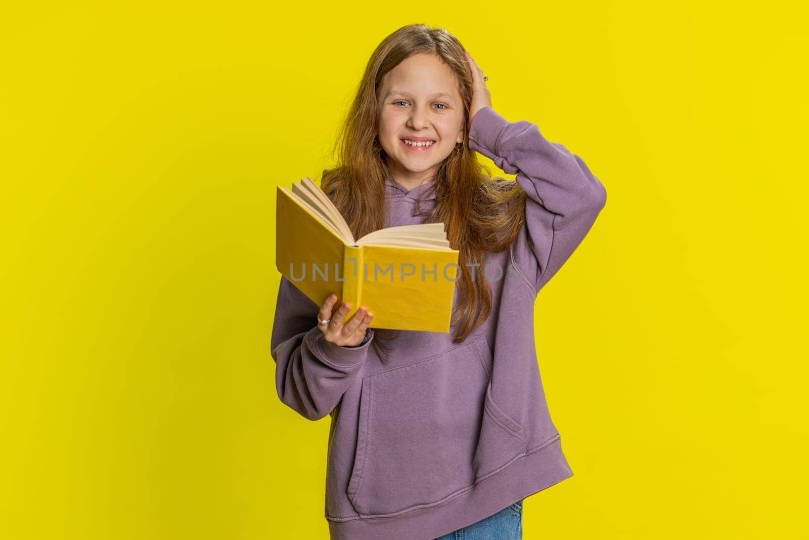 Happy relaxed smiling preteen child girl kid reading funny interesting fairytale story book, leisure hobby, knowledge wisdom, education, learning, study, wow. Children isolated on yellow background