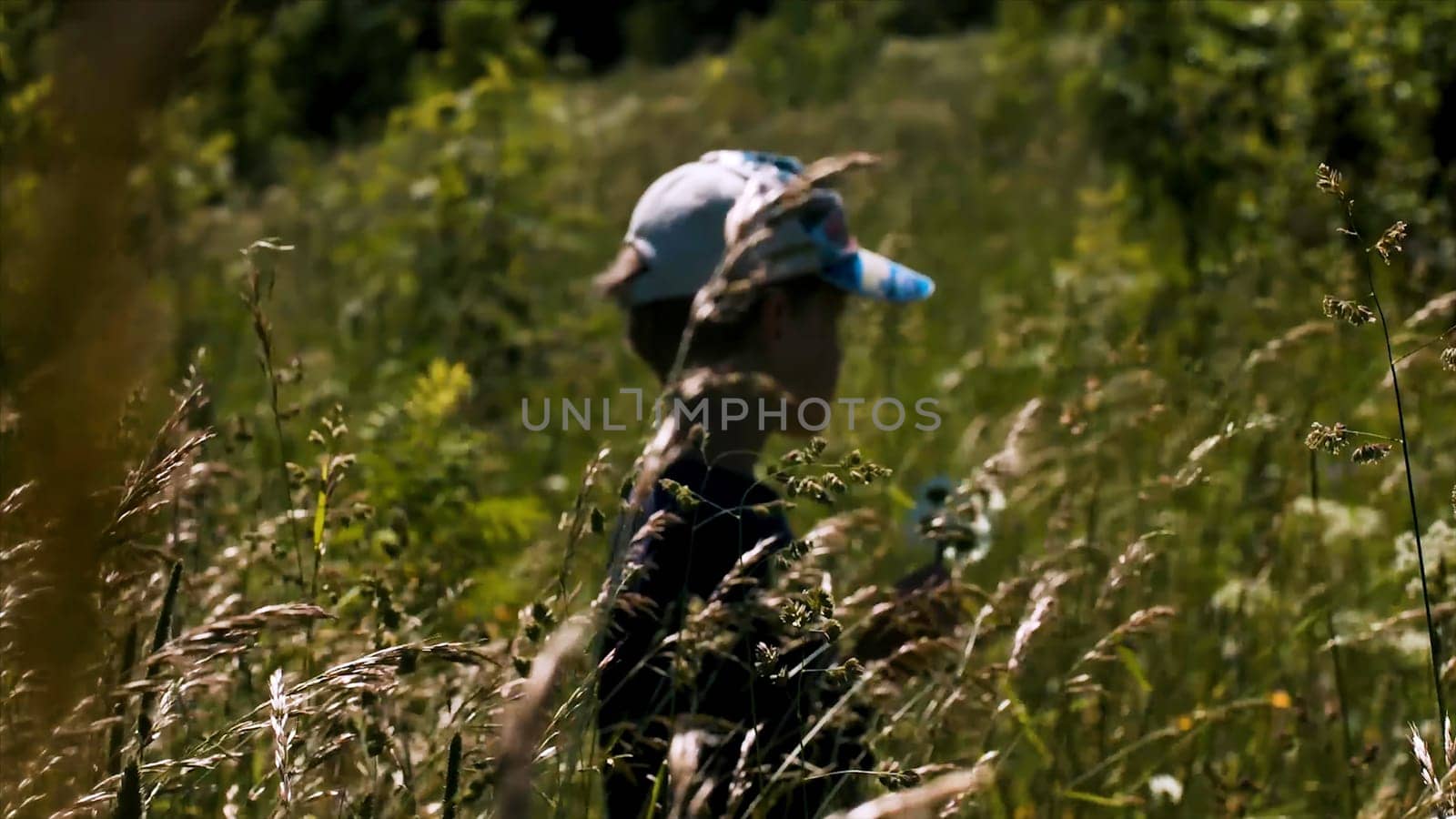 Portrait of a thoughtful little boy standing in long grass. Creative. Cute boy child in the summer meadow under the shining sun