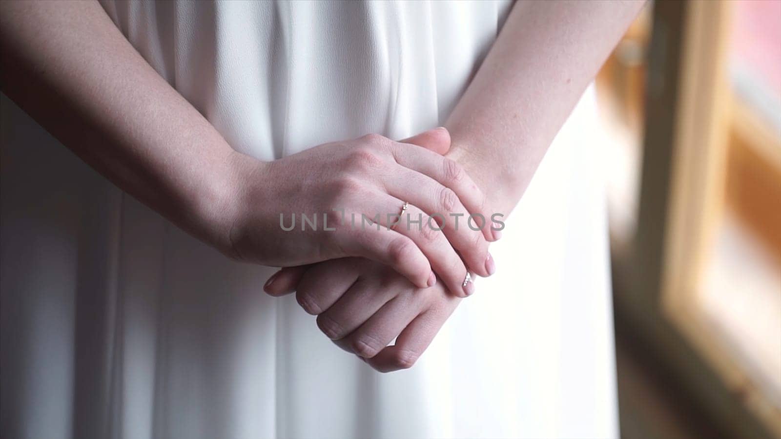 Girl in white dress staying near the window. Girl's hand with wedding ring or engagement ring. Beautiful young woman in white dress stay near the window at home.Elegant. Morning of the bride. Beautiful young woman in white negligee staying near the window HD
