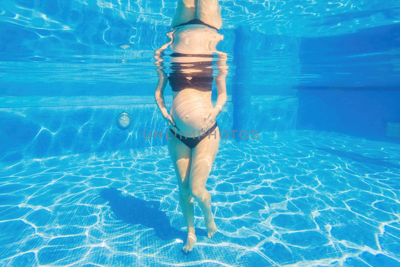 Pregnancy embraced underwater a tranquil scene as a woman tenderly hugs her belly in the pool, capturing the beauty of maternal connection.