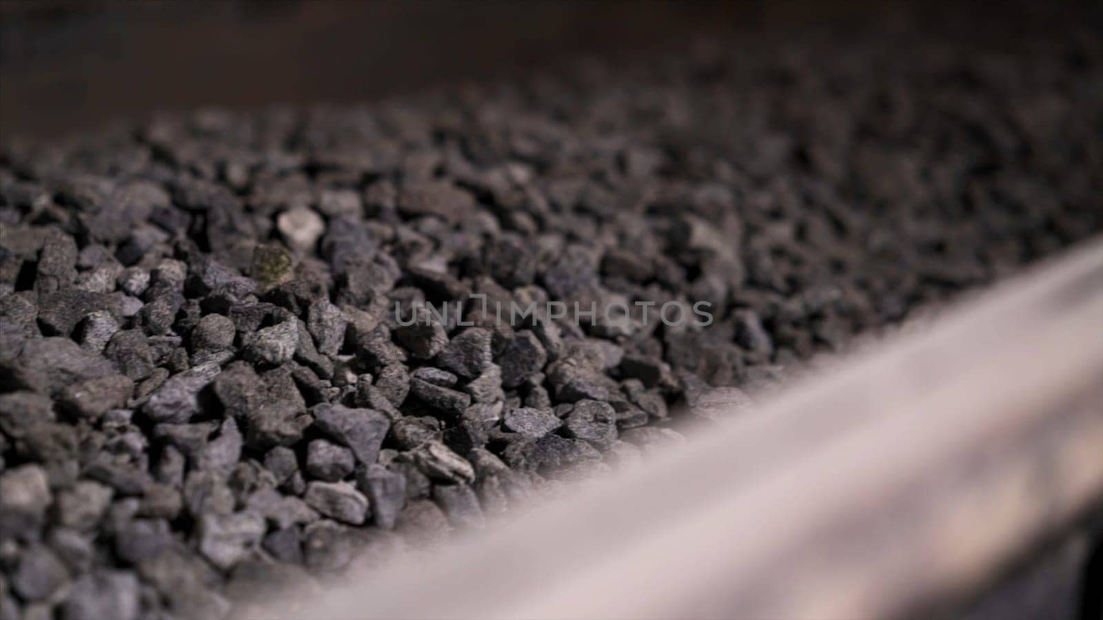 Close up of crashed stones transportation by conveyor to produce construction materials. Moving production line with macadam, industrial background.