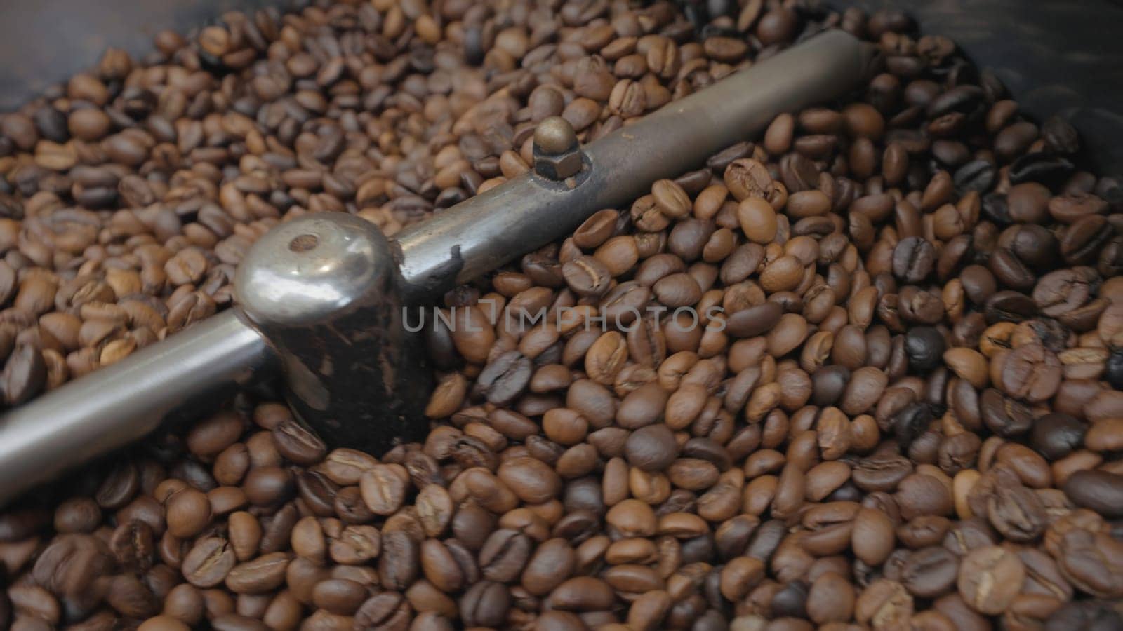 Roasting of coffee beans at factory. Action. Coffee beans are mixed in industrial machine during roasting. Industrial roasting of coffee in special equipment.