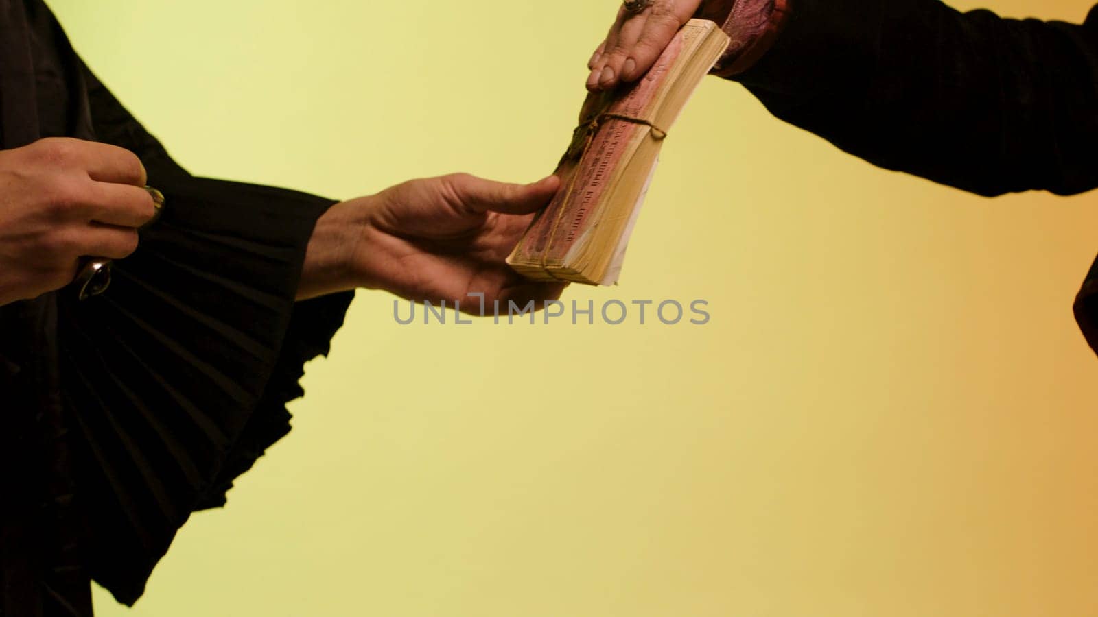Close up for eastern woman hand giving a pile of money to seller and getting round, silver watch, isolated on yellow background, time is money concept. Woman gets silver watch for paper money.