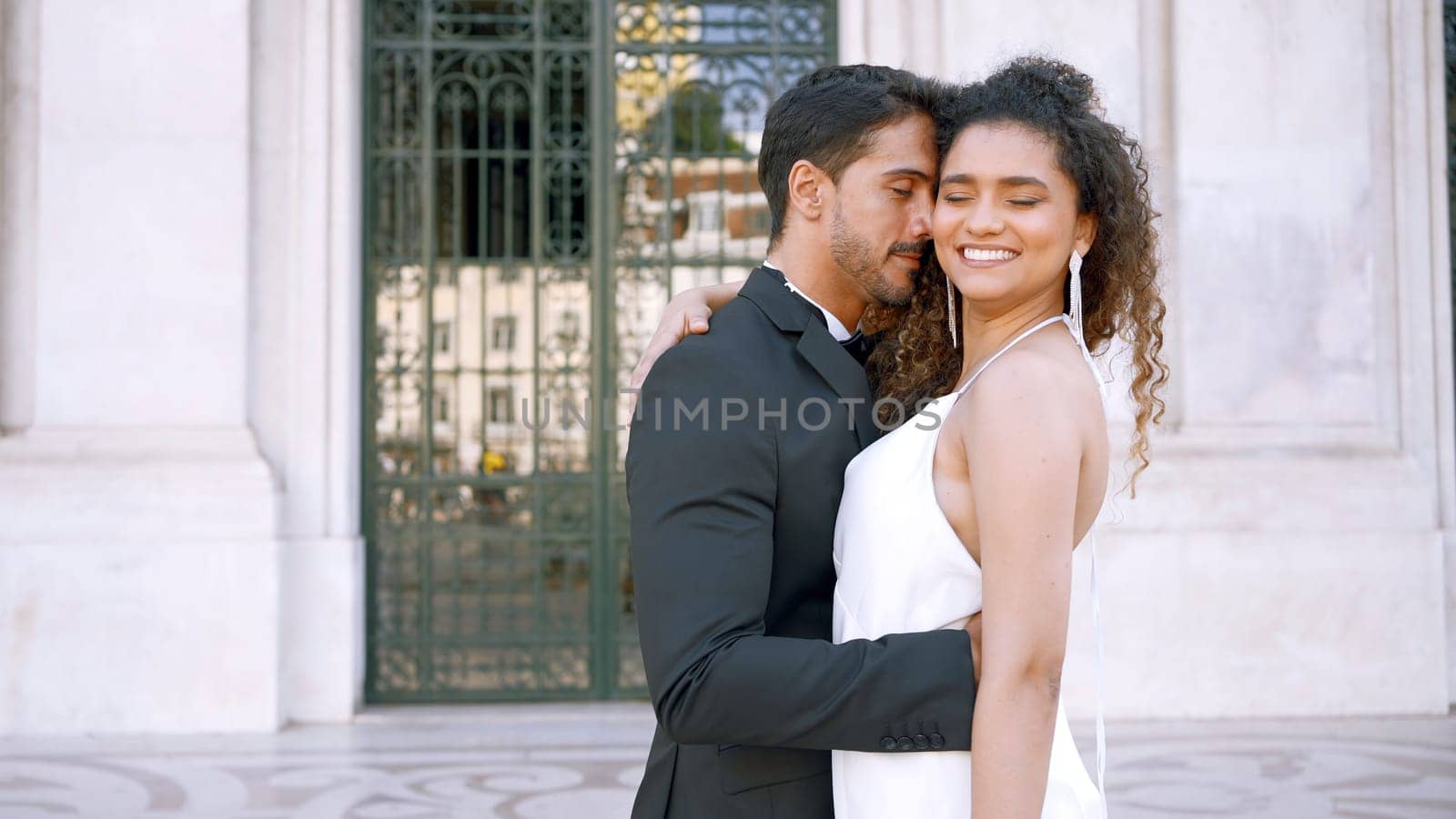 Beautiful couple in outfits happily embracing. Action. Attractive couple in luxurious outfits on street of old town. Gorgeous young couple happily embraces on sunny day.