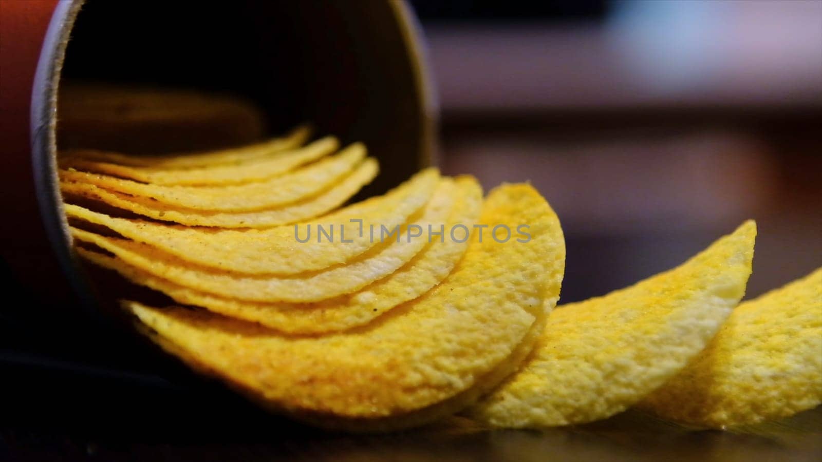 Close up of potato chips put out of can on the table on blurred background. Hand taking delicious snack, concept of unhealthy diet.