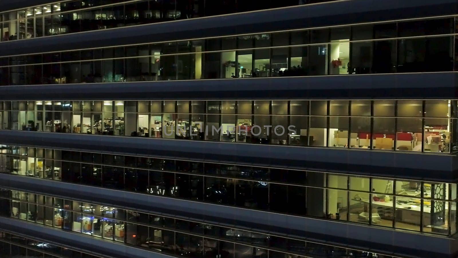 Close up for exterior of modern office building corner with lighted windows and people inside. Aerial of the downtown office building corner at night, lighted windows background.