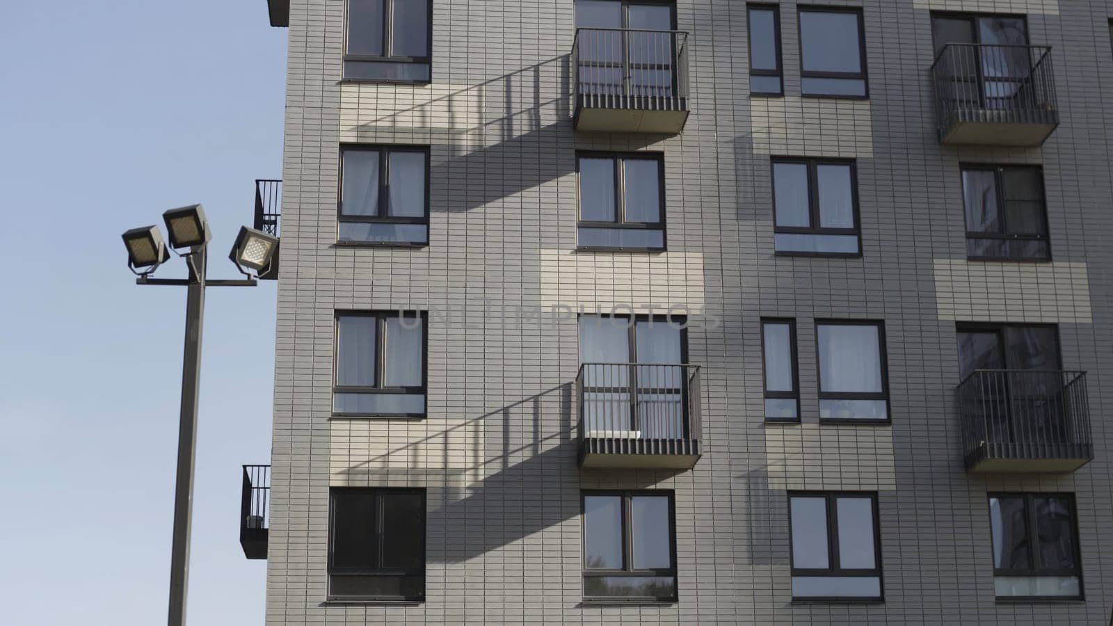 Bottom view of residential new building made of white bricks. Fragment of a white brick new apartment house with balconies and street lanterns against a clear sky.