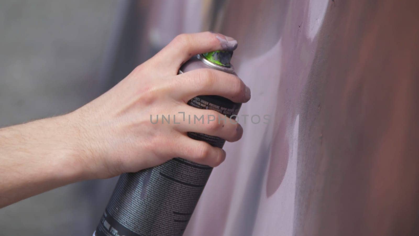 A hand with a spray can that draws a new graffiti on the wall. Photo of the process of drawing a graffiti on a wooden wall close-up. The concept of street art and illegal vandalism 4K