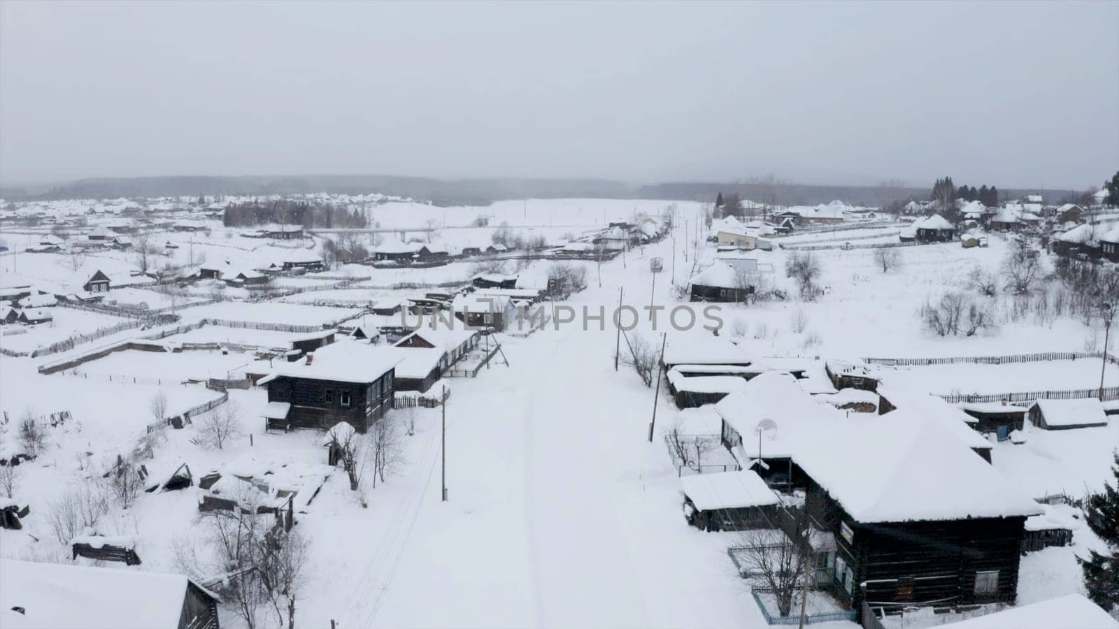 Aerial view of snow covered roofs of wooden houses. Clip. Small winter village on a heavy cloudy sky background