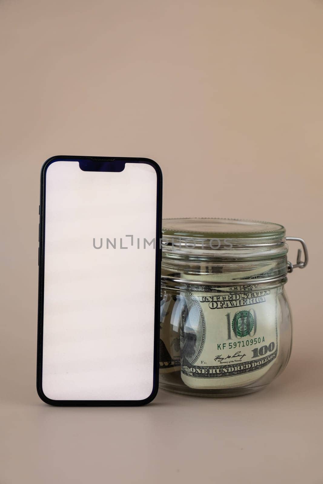 White smartphone screen mock up template in vertical position on beige background. Copy space App website advertising. Jar filled with dollars cash. Concept of Mobile application and technology business savings.