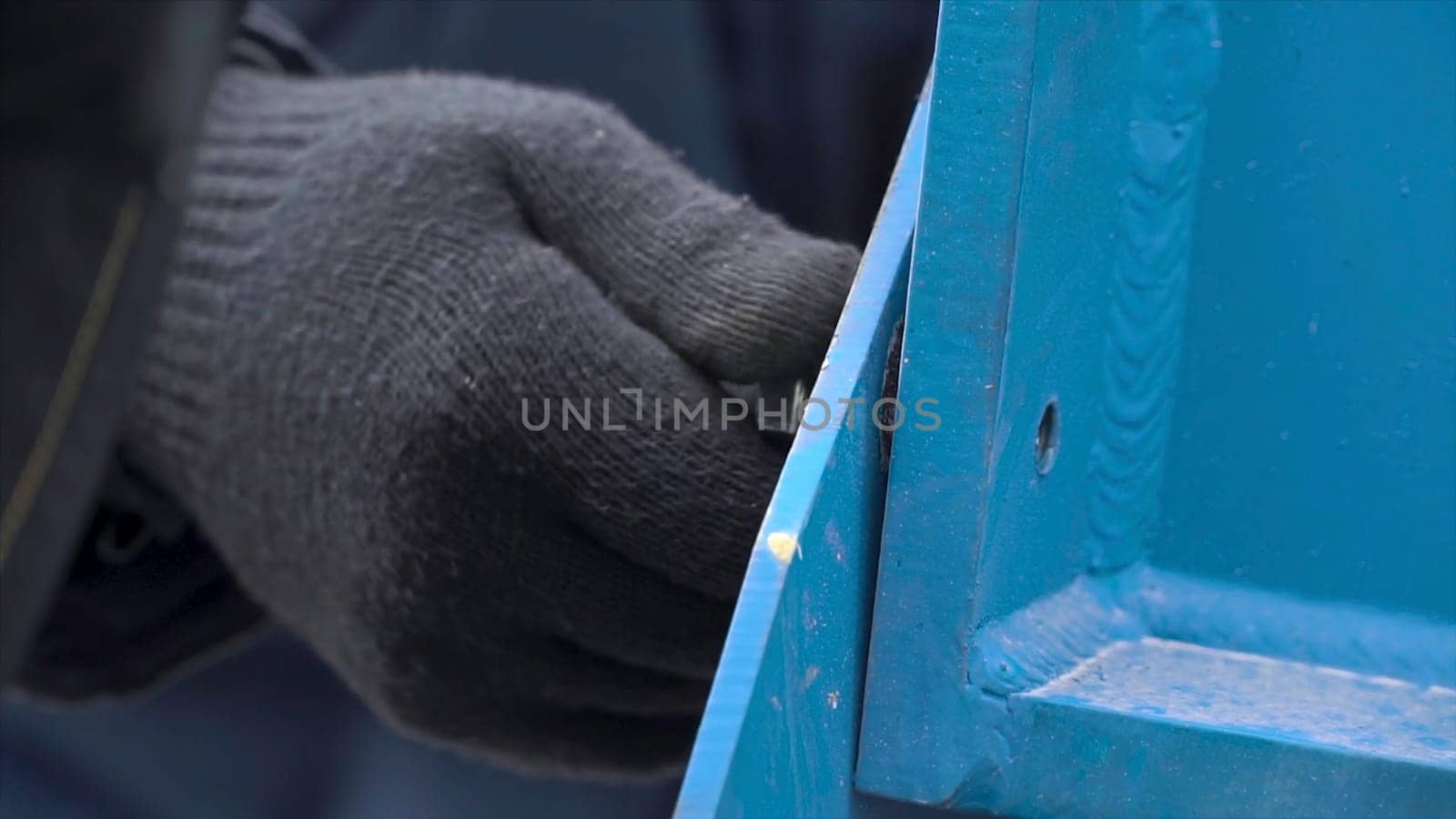Close up for man hands in protective gloves loosening the bolt with a wrench on the metal blue structure. Dismantling of the metal construction.