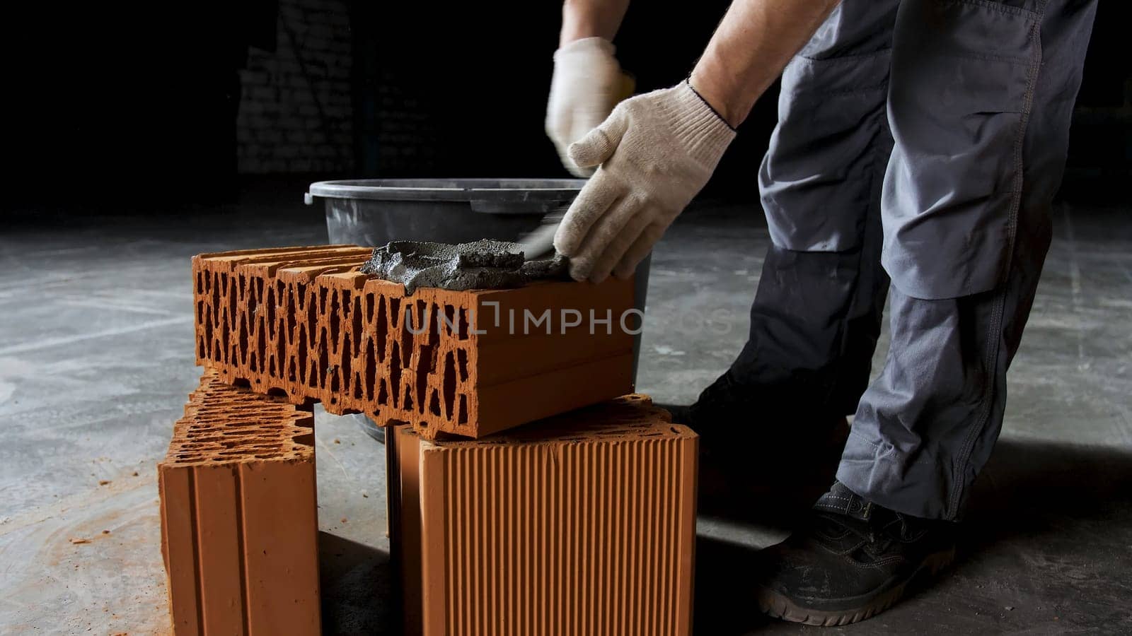 Close up of an industrial worker putting cement on the brick for construction work. Hands of a man putting mortar on red brick, materials and construction concept.