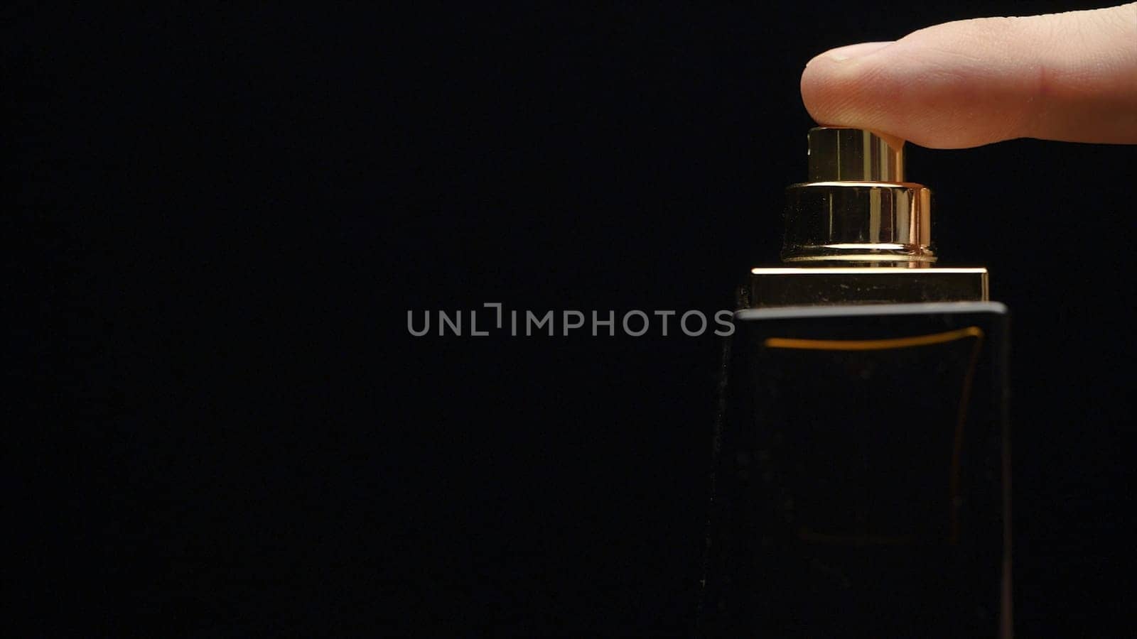 Fragrance luxury bottle contents in dark spraying slow motion. Perfume bottle spray on black background. Spraying Cologne on a black background. lose up of handsome young business man using perfume or deodorant on black background macro.