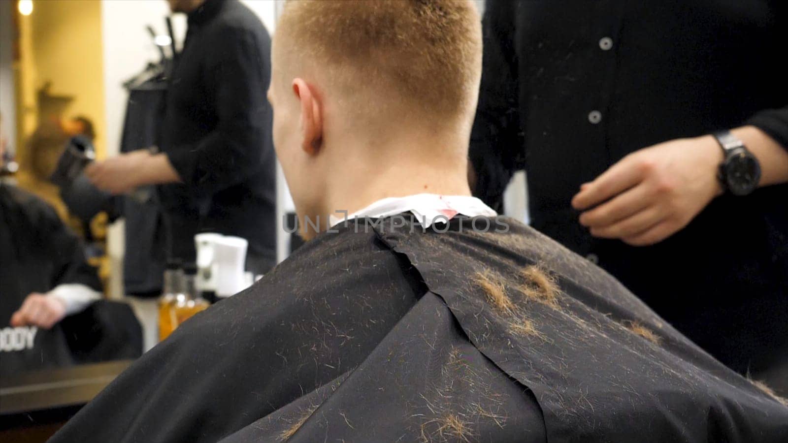 Barber cutting hair with scissors and hair flying in the air in slow motion. Back view of man in barber shop and flying hair in slow motion. Close-up back view of young bearded man getting beard haircut by hairdresser at barbershop