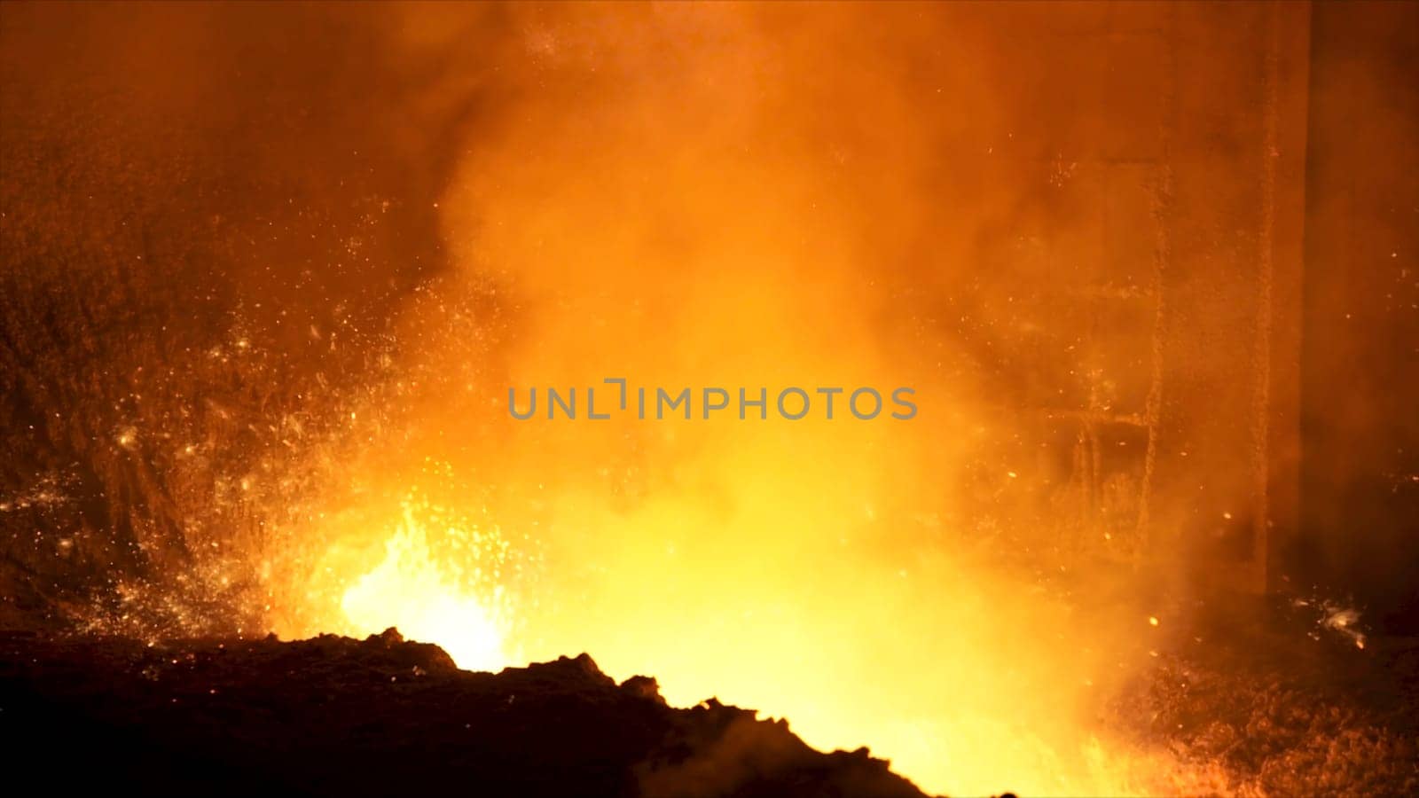 Close up of liquid metal in hot workshop of the metallurgical plant. Flying sparkles inside the furnace, heavy industry concept.