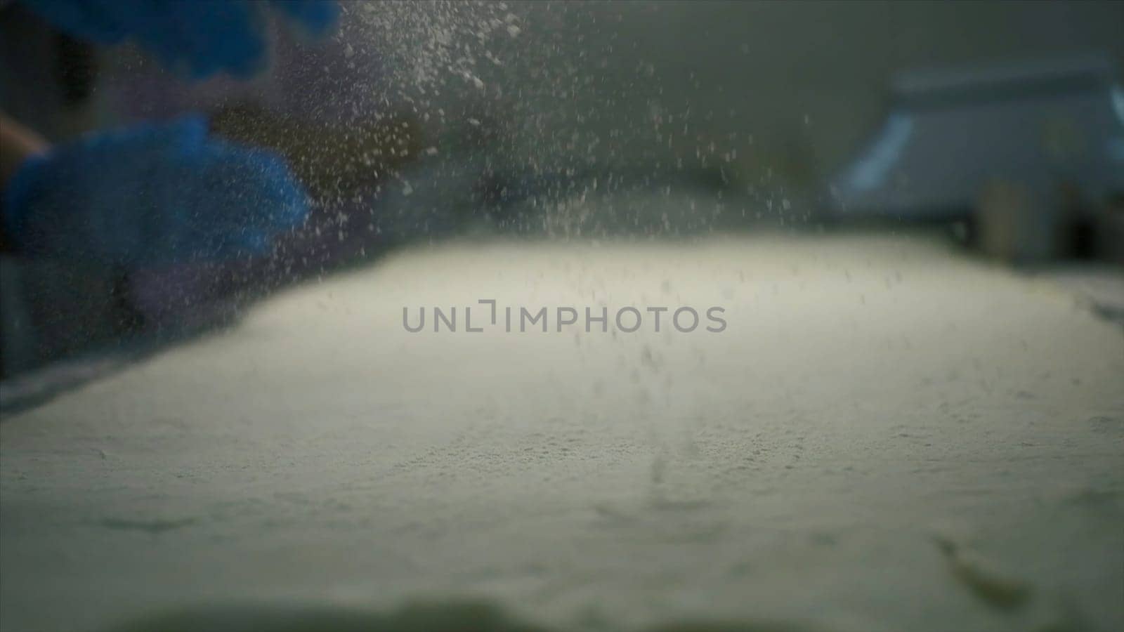 Close-up of sprinkling flour during cooking. Clip. Cook sprinkles flour on cooking table. Sprinkling flour for baking. Production bakery.