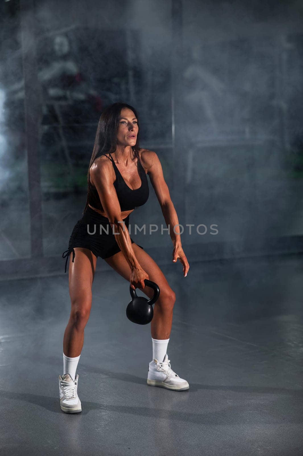 A beautiful brunette with big breasts does Russian swings with a kettlebell. Vertical photo