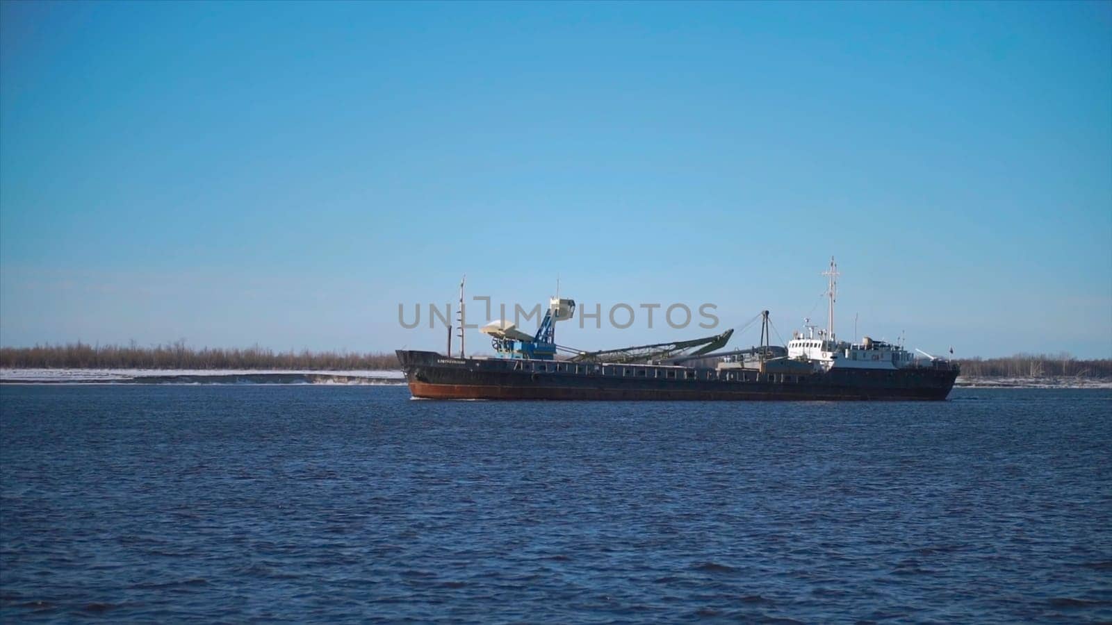 Cargo ship sailing on river on clear day. Clip. Merchant ship or barge sails along river. Commercial and industrial shipping.