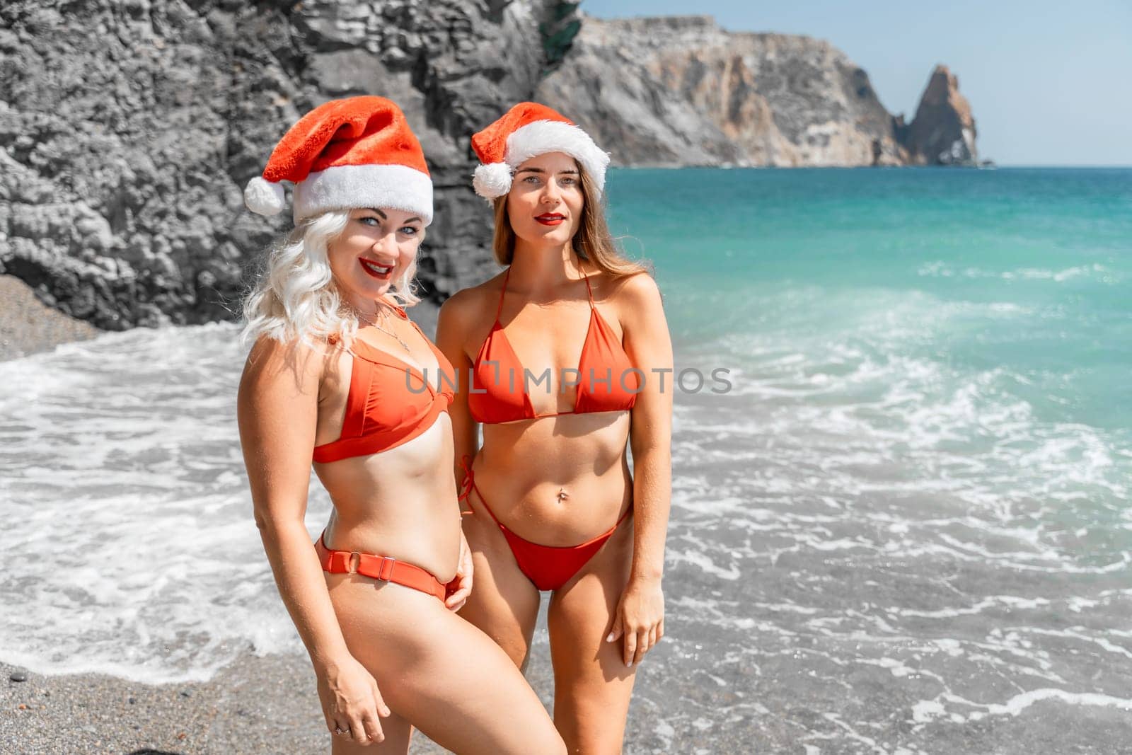 Women in Santa Claus hats run into the sea dressed in red swimsuits. Celebrating the New Year in a hot country.