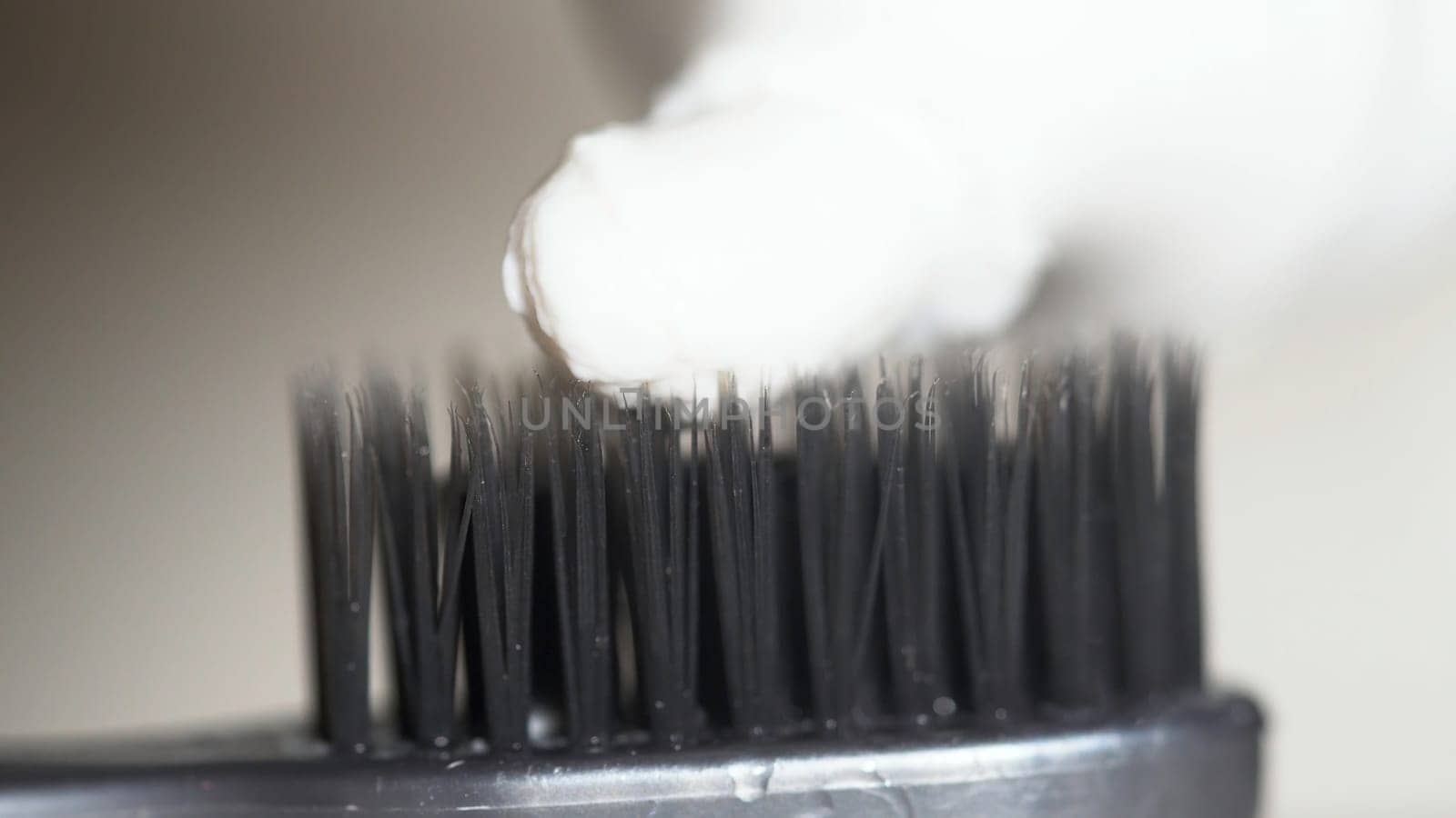 Extreme close up for a black toothbrush with white toothpaste being squeezed on it on beige background. The black bristles of the toothbrush with white toothpaste, dental care concept.
