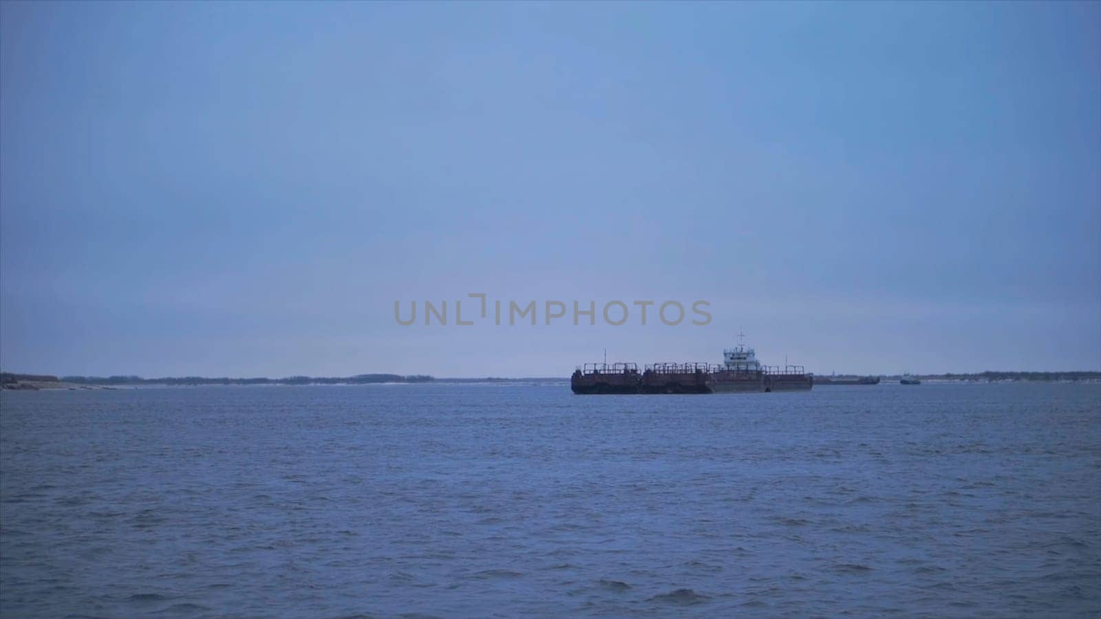 Barge floating on river on cloudy day. Clip. Beautiful river landscape with floating merchant ship. Barge crossing on river on cloudy day.