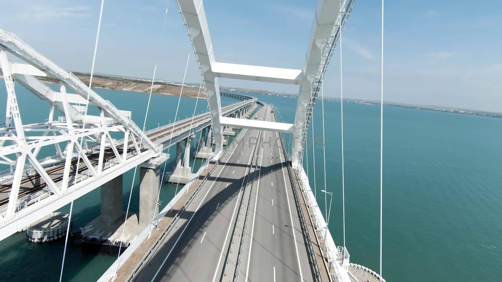 Huge bridge. Drone view. Action. A long bridge over the ocean on which cars can move freely, the bridge is located next to the green mountains.