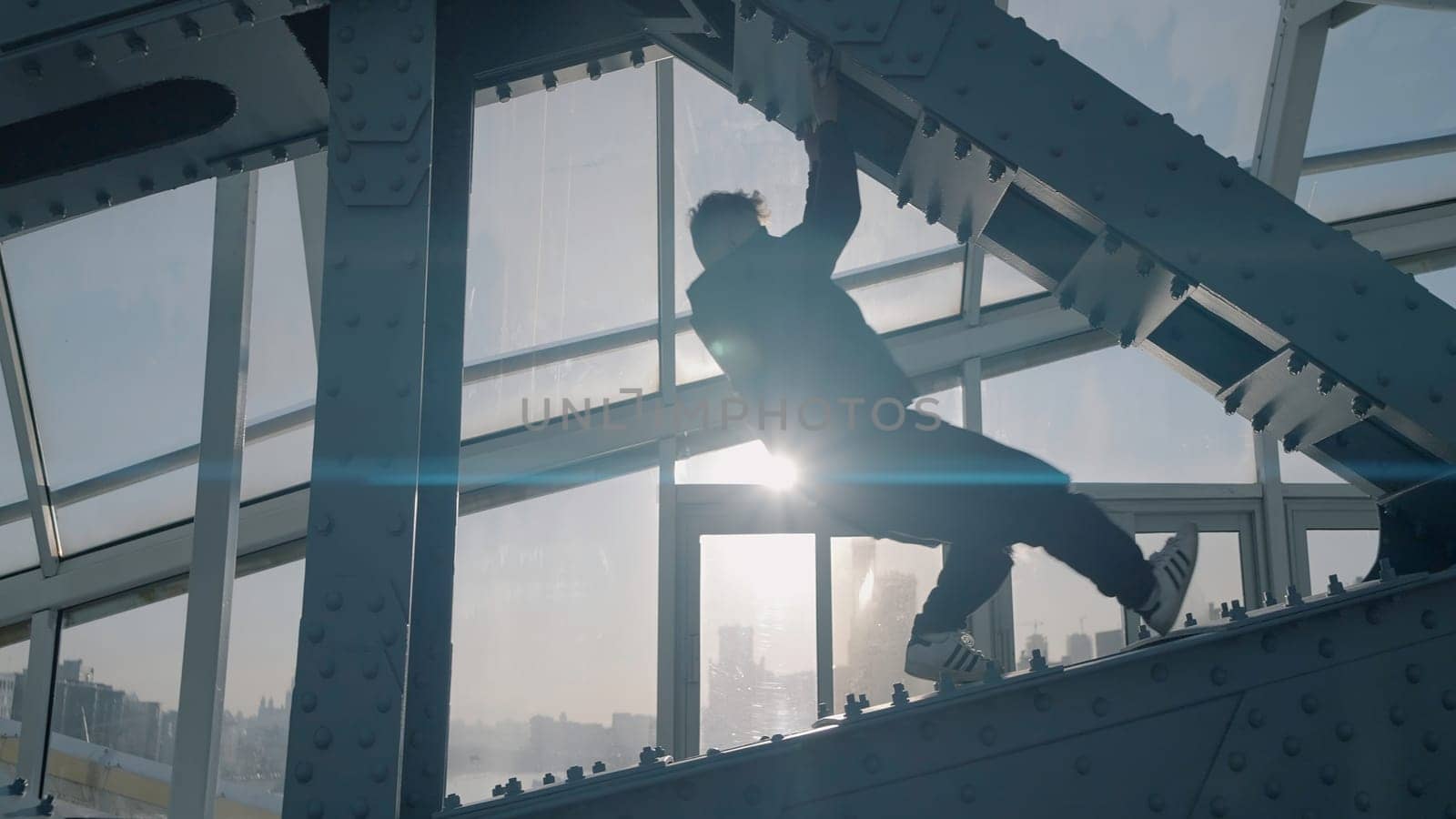 Young man dances on bridge on background of sun. Action. Young man is dancing on modern building structure.