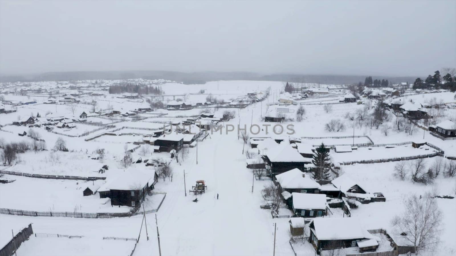 Aerial view of snow covered roofs of wooden houses. Clip. Small winter village on a heavy cloudy sky background