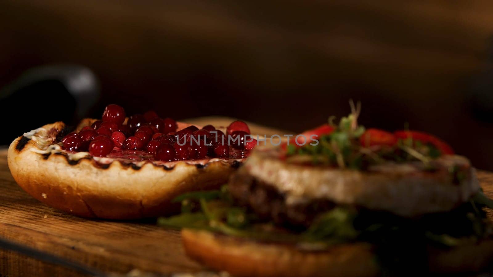 Close up of hamburger sandwich with cutlet of minced meat, cheese brie, camembert, berry cherry sauce. Male chef putting top burger bun on the other ingredients, foodporn and fast food concept.