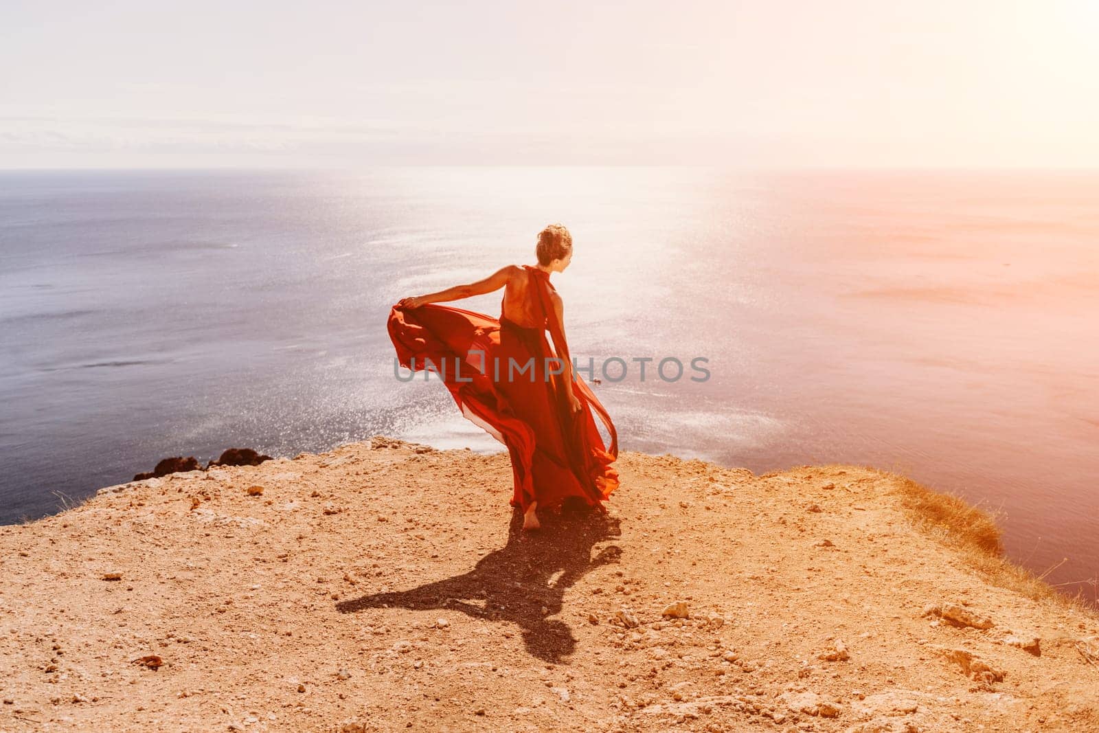 Woman red dress sea. Female dancer in a long red dress posing on a beach with rocks on sunny day. Girl on the nature on blue sky background. by Matiunina