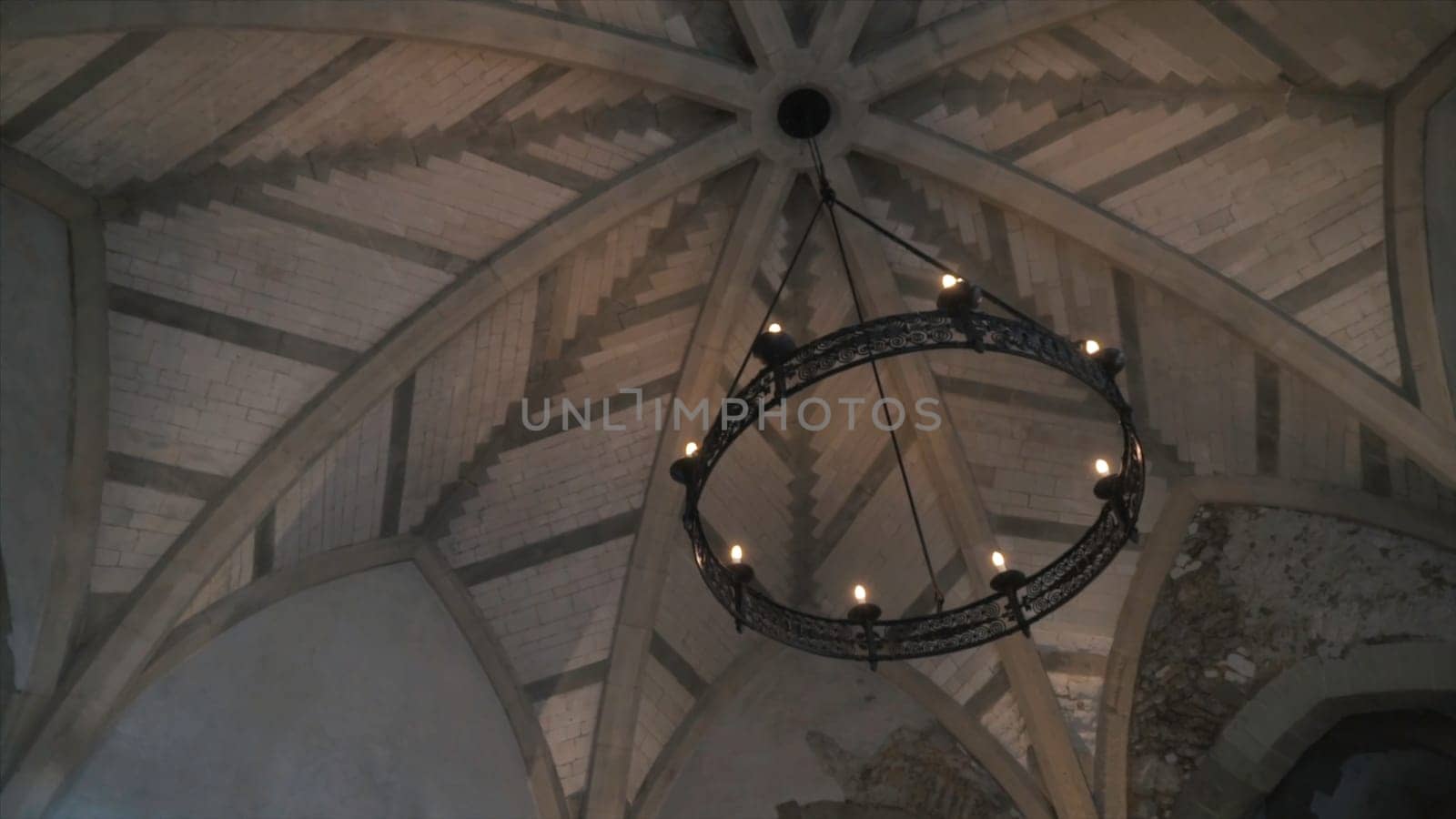 View from the bottom on the old chandelier in the form of a wheel with light bulbs hanging on the ceiling in church or another old building. Beautiful retro style