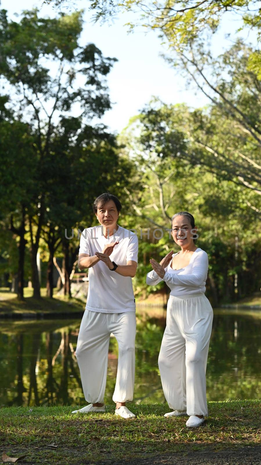 Full length view of active retired senior couple practicing traditional Tai Chi outdoors near lake. by prathanchorruangsak