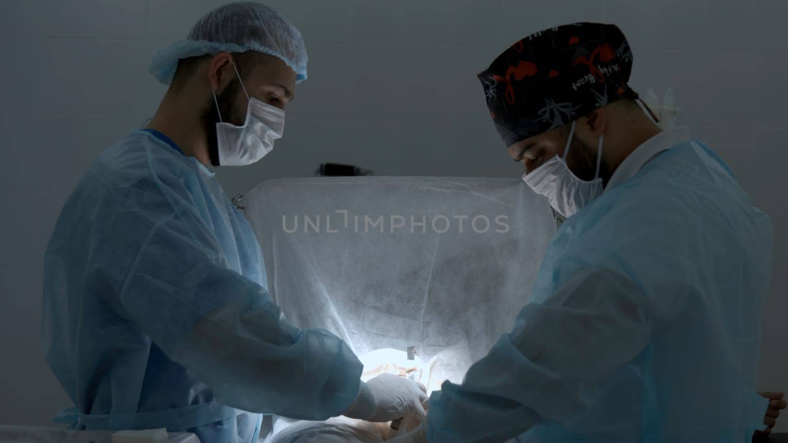 Surgeons working in operating room at a hospital. Action. Two male doctors at work. by Mediawhalestock