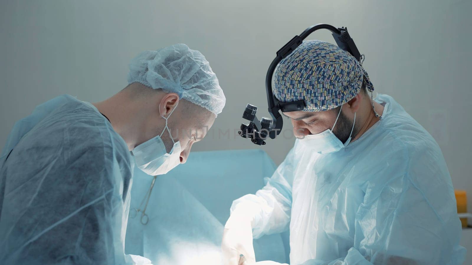 Two surgeons busy at work . Action . Two men in blue lab coats are painstakingly working on a complex operation , using various medical accessories like microscopic glasses . High quality 4k footage