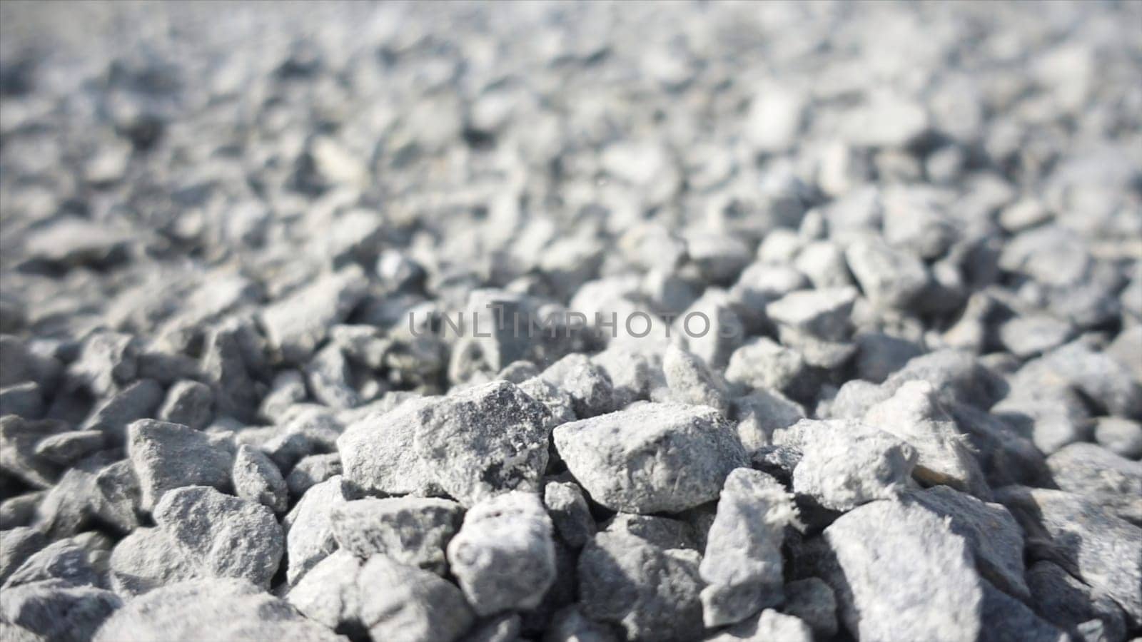 Background of gray granite gravel under the bright sun. Close up of white stones falling down on the ground, pebble texture.