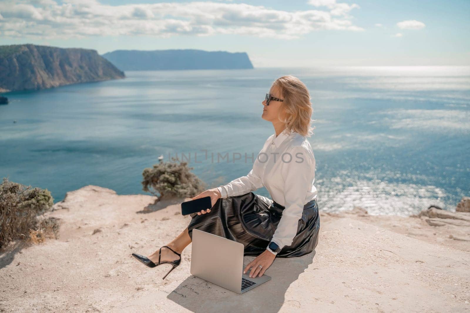 Freelance women sea. She is working on the computer. Good looking middle aged woman typing on a laptop keyboard outdoors with a beautiful sea view. The concept of remote work