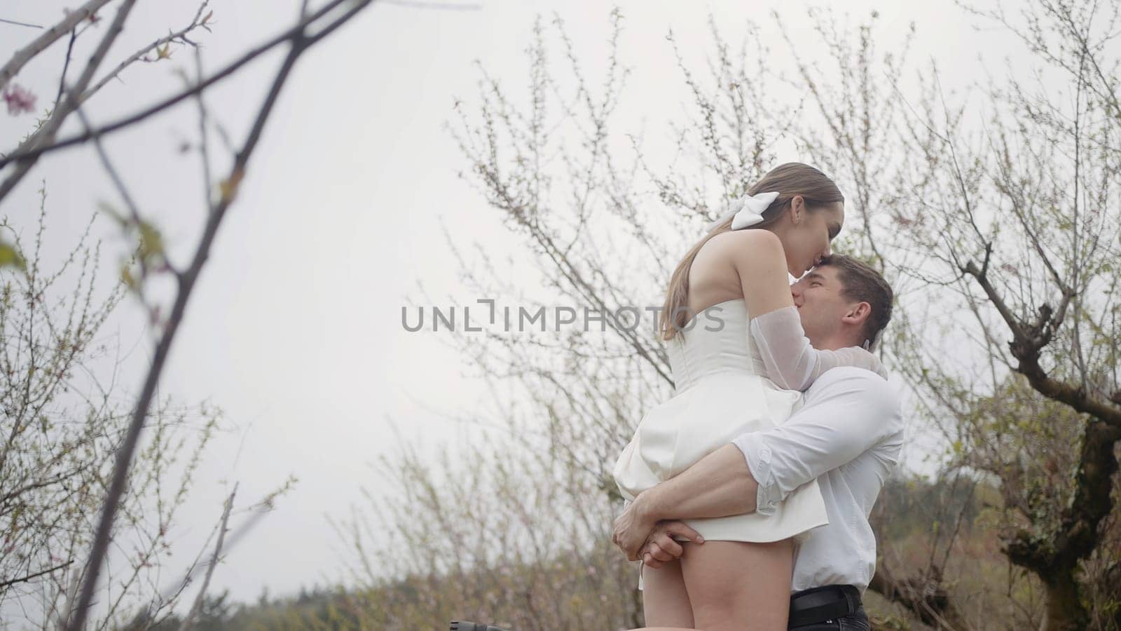 Beautiful couple embraces in spring garden. Action. Couple of newlyweds enjoy first leaves and flowers in garden in spring. Couple embraces in blooming garden in early spring.