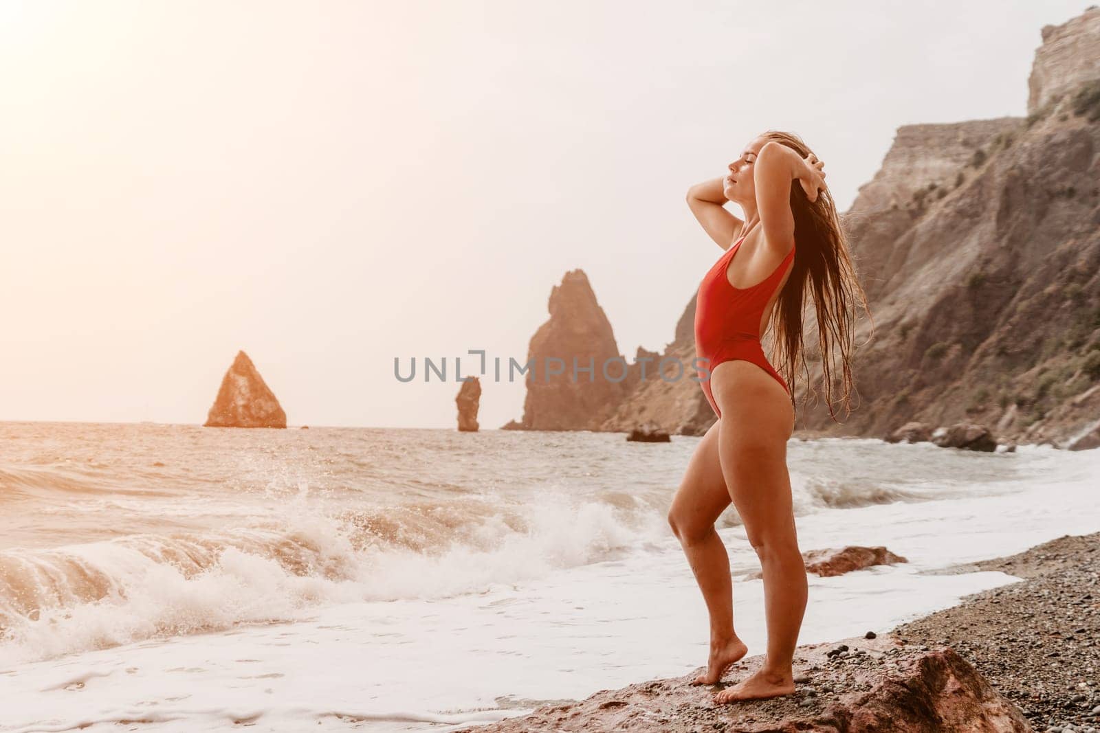 Woman travel sea. Young Happy woman in a long red dress posing on a beach near the sea on background of volcanic rocks, like in Iceland, sharing travel adventure journey