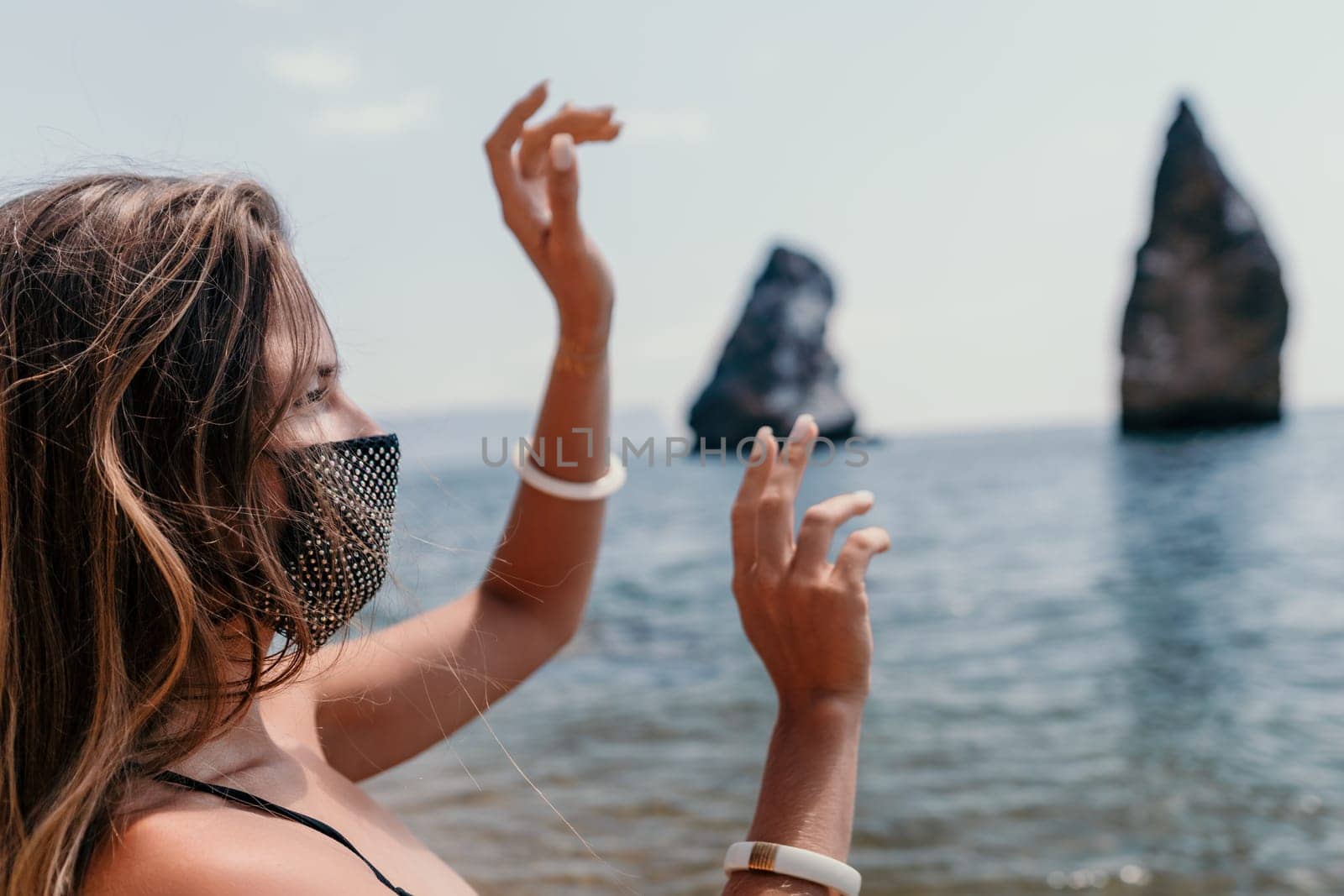 Woman summer travel sea. Happy tourist in black mask enjoy taking picture outdoors for memories. Woman traveler posing on the beach at sea surrounded by volcanic mountains, sharing travel adventure by panophotograph
