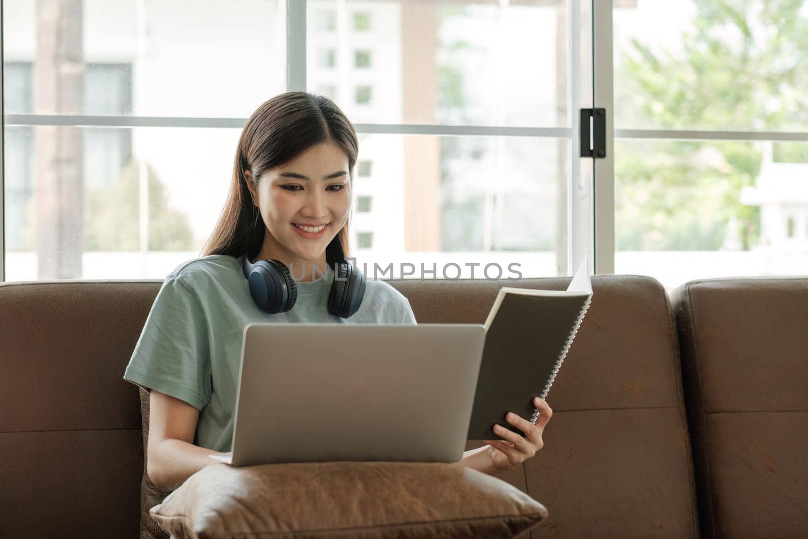 Young female student wearing headphones sits intently and happily studying online on her laptop on the sofa in the living room at home..