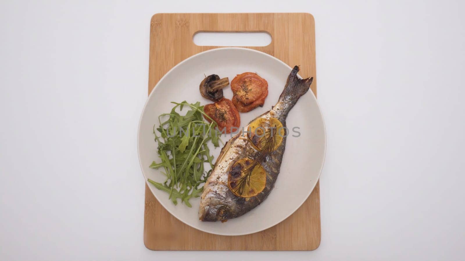 Baked fish with lemon and spices in restaurant. Action. Beautifully served fish in restaurant on white background. Simple elegant serving of baked fish on white plate.